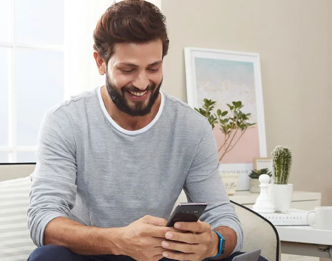 A smiling man looking at a phone while sitting on a couch