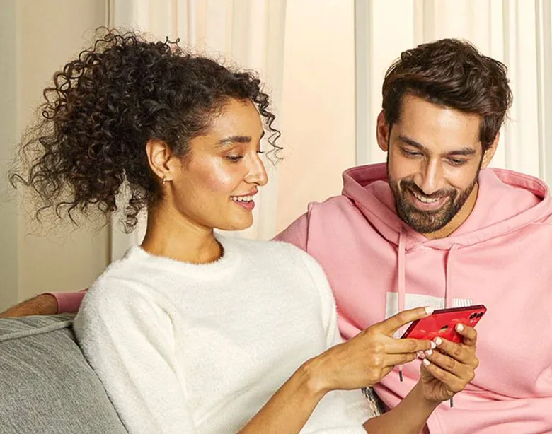 Um casal sentado no sofá olhando para o celular