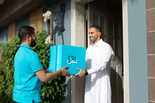 A man standing at the front door, receiving a package from a SPL delivery person