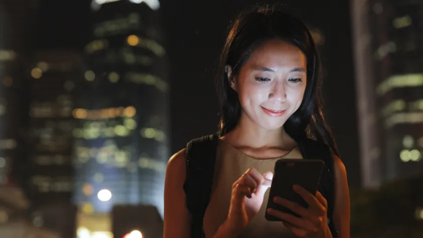 Person walking through city at night while looking at phone. The phone light is shining bright on their face.