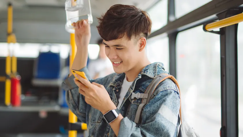 Person standing on bus while smiling at a WhatsApp business message on phone