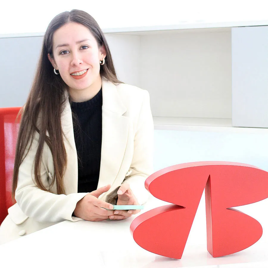 Uma mulher vestida formalmente segurando um celular, sorrindo para a câmera