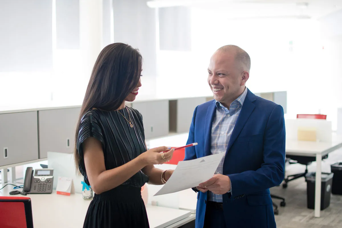 A man and a woman holding a paper document, smiling and talking