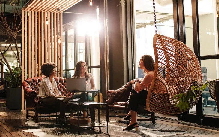 Community workplace with a person working on laptop and a conversation happening amongst coworkers