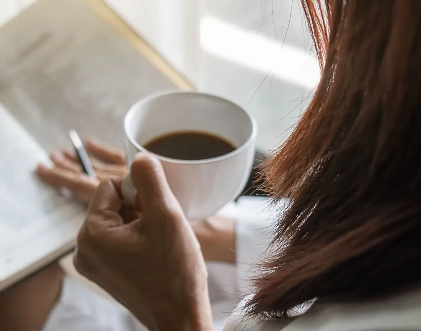 Una persona inmersa en la lectura de un libro, mientras sostiene una taza de café