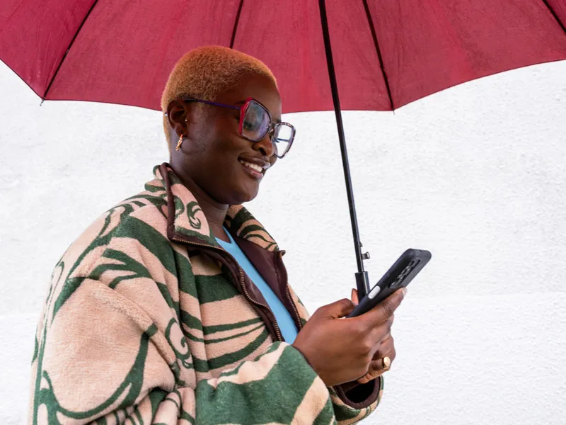 Uma mulher segurando um guarda-chuva e olhando para o smartphone