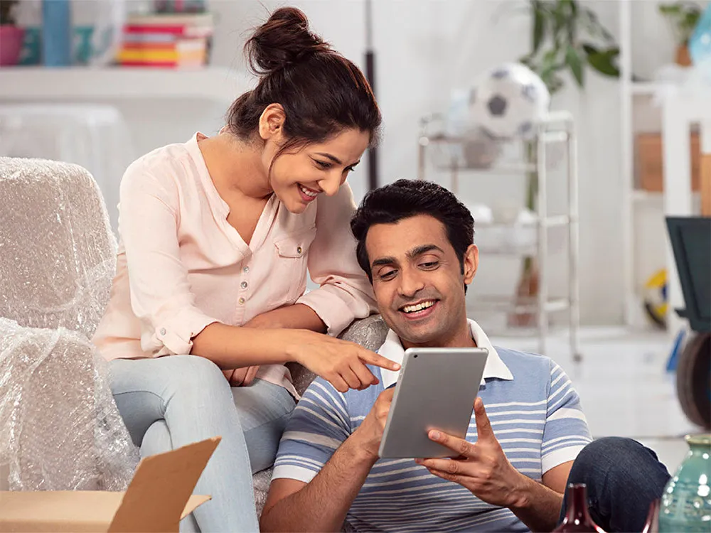 Un homme et une femme souriant en regardant une tablette.