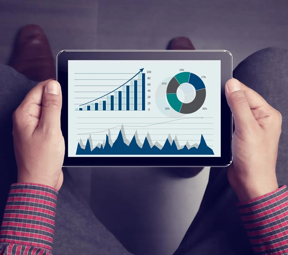 Um homem segurando um tablet e observando métricas e gráficos de marketing