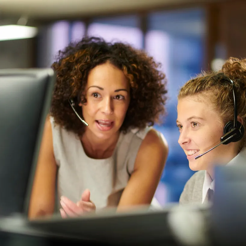 Dos mujeres con auriculares observan el monitor de una computadora que tienen delante de ellas